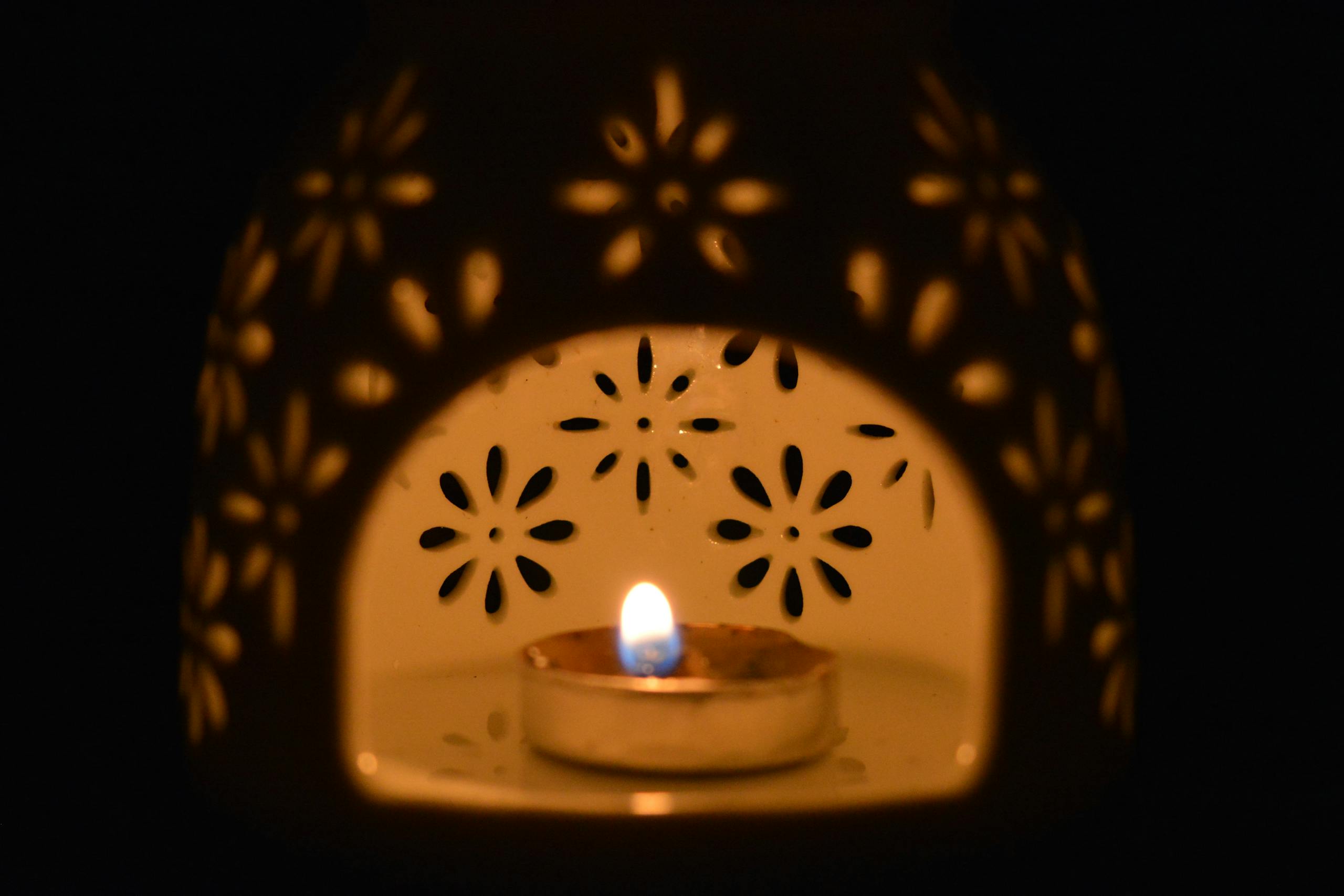 A close-up of a decorative ceramic candle holder with a burning tealight inside, creating a warm floral pattern.