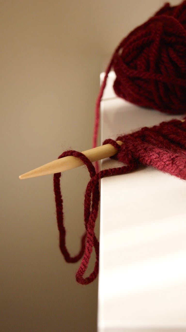 A detailed image of burgundy yarn with knitting needles, ideal for craft and hobby themes.