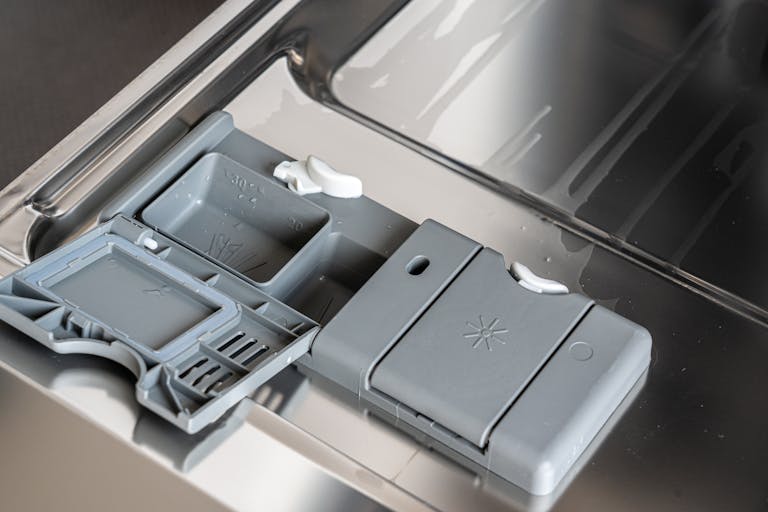 A detailed view of a dishwasher detergent compartment with soap residue.