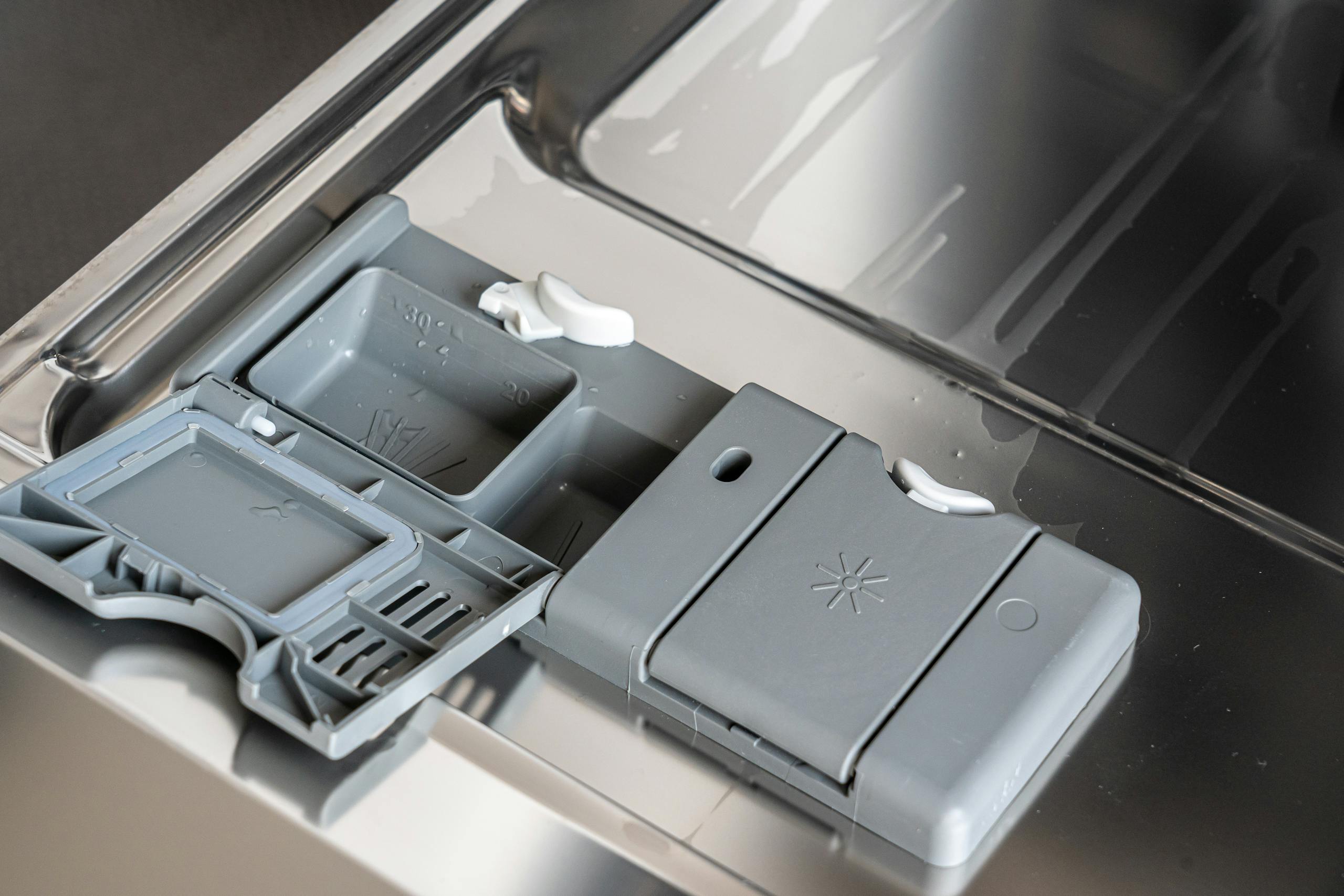 A detailed view of a dishwasher detergent compartment with soap residue.