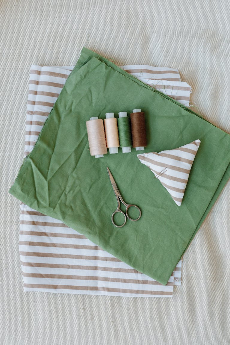A flat lay of sewing tools and striped fabric with scissors and threads.