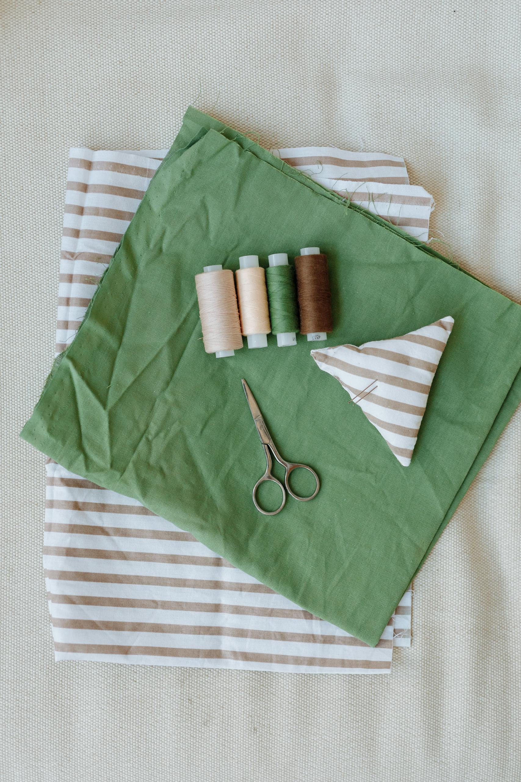 A flat lay of sewing tools and striped fabric with scissors and threads.