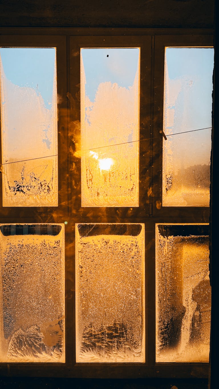 A frosty window glowing with warm sunlight during a winter sunrise, creating a beautiful contrast.