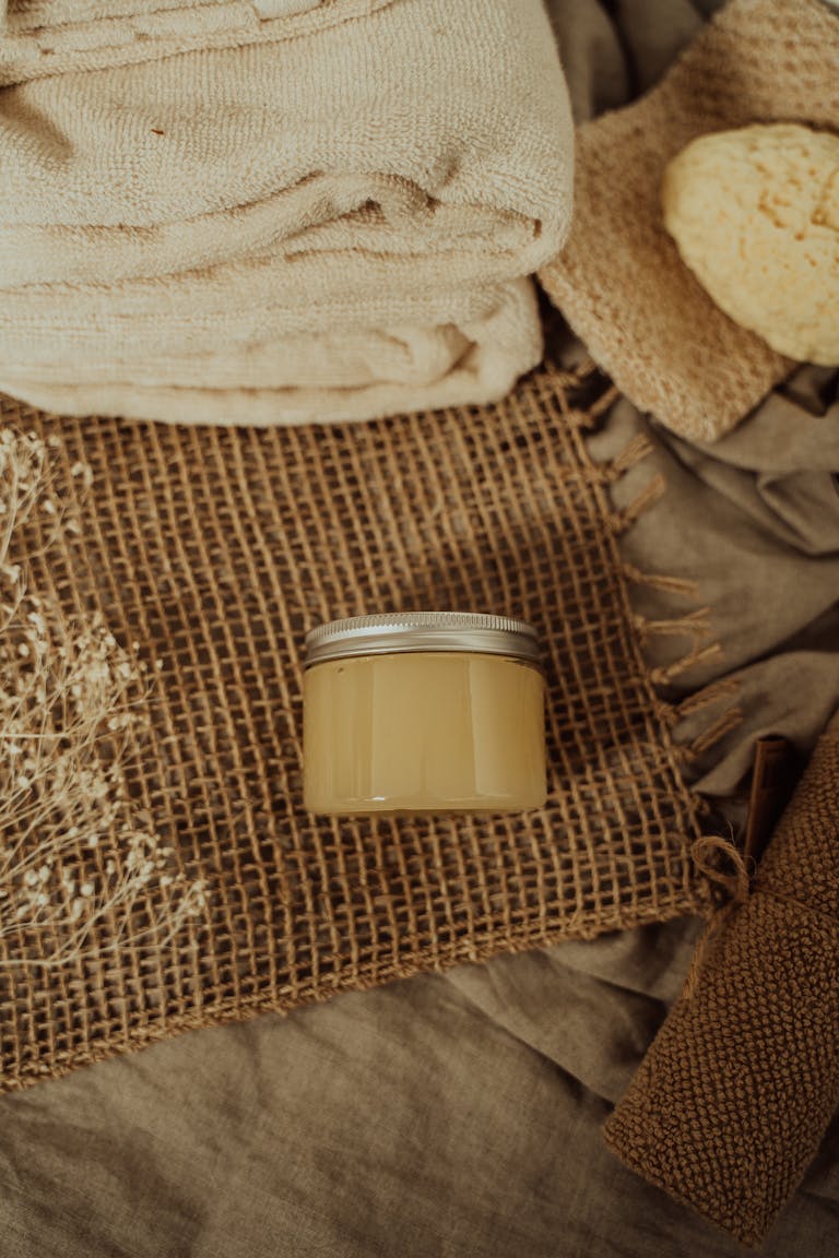 A natural spa-themed flatlay showcasing towels, scrub, and a small container on burlap and linen.