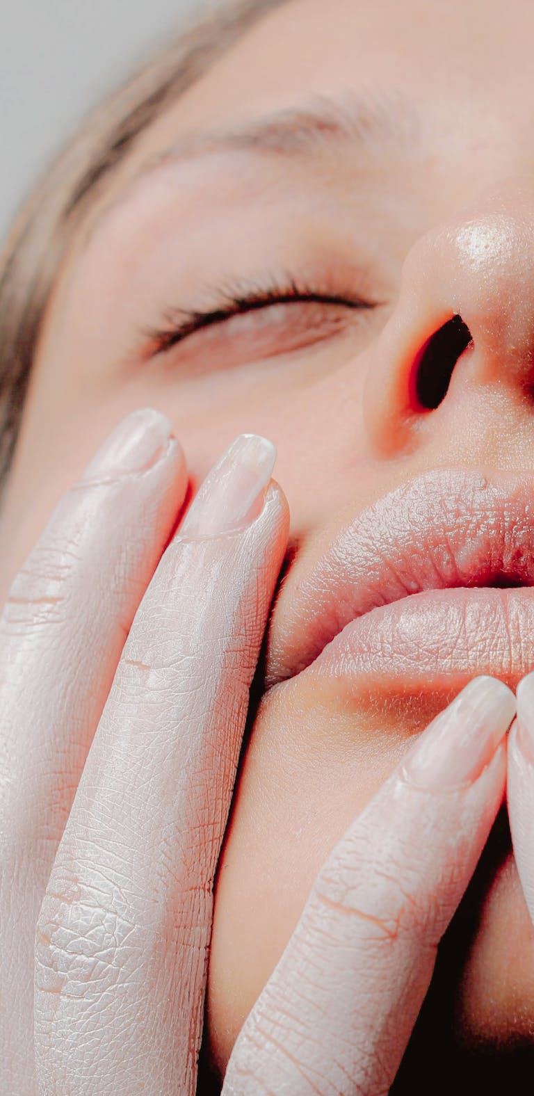 A serene close-up portrait of a woman with softly touching hands on her face.