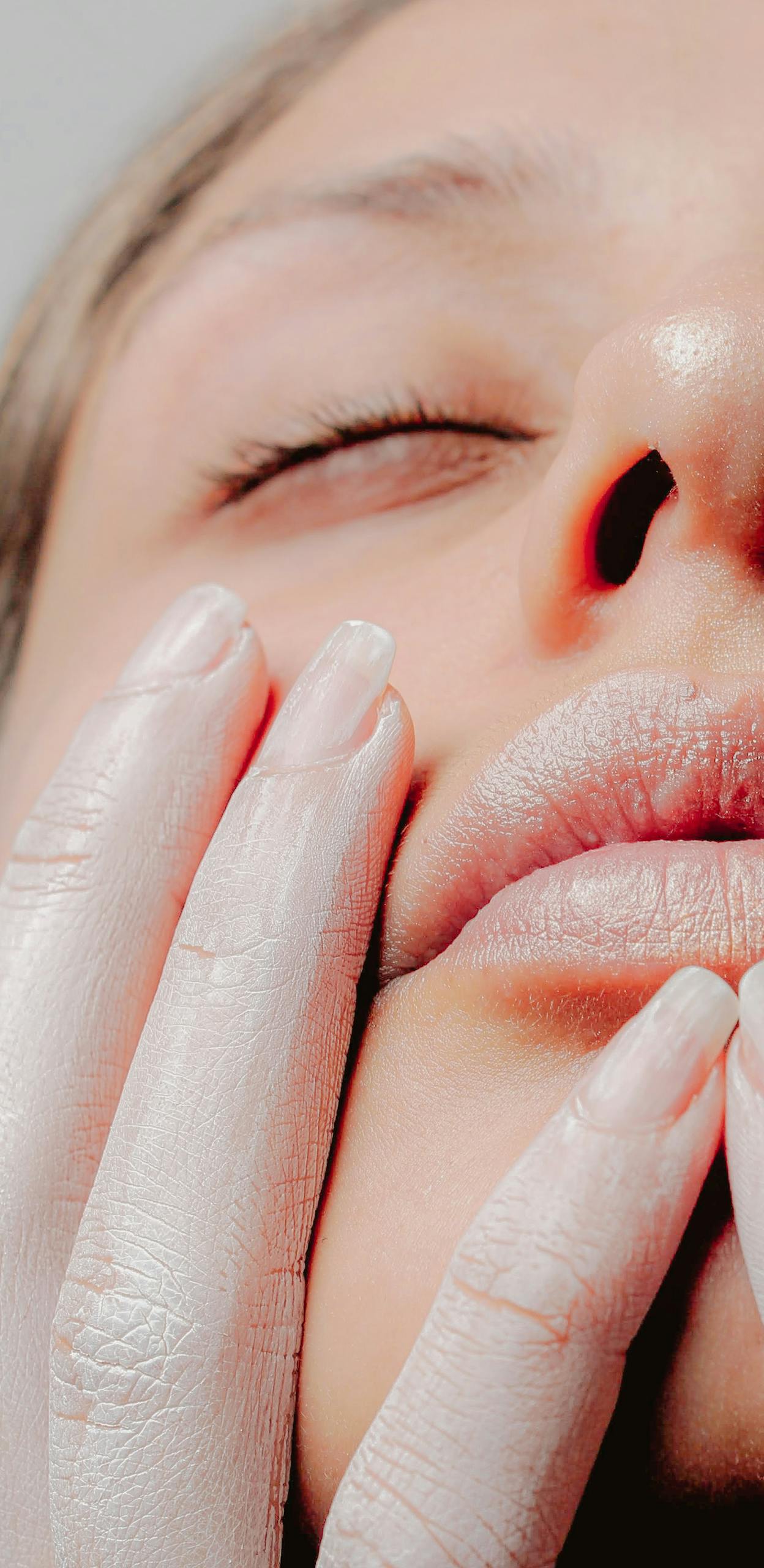 A serene close-up portrait of a woman with softly touching hands on her face.