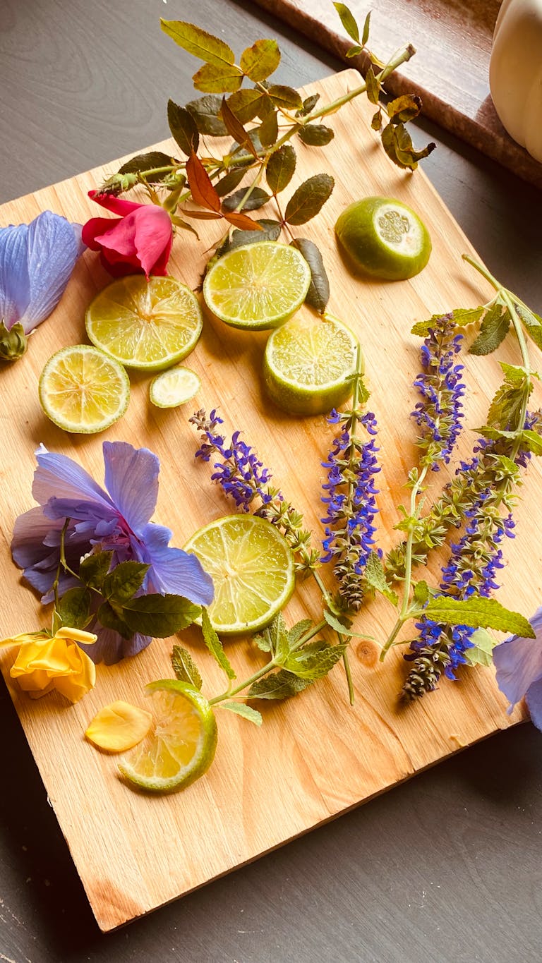A vibrant arrangement of lime slices and colorful flowers on a wooden board, captured in natural light.