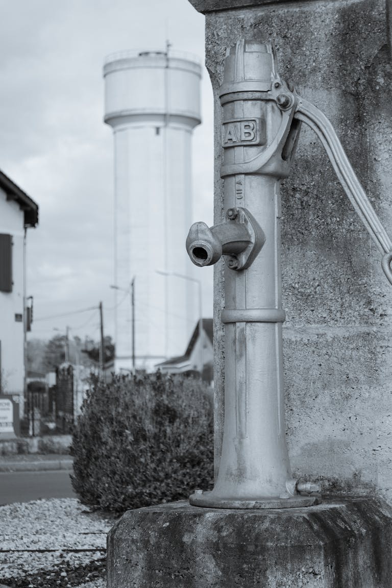 A vintage water pump with a water tower in Saint-Aigulin, France, illustrating rustic charm.