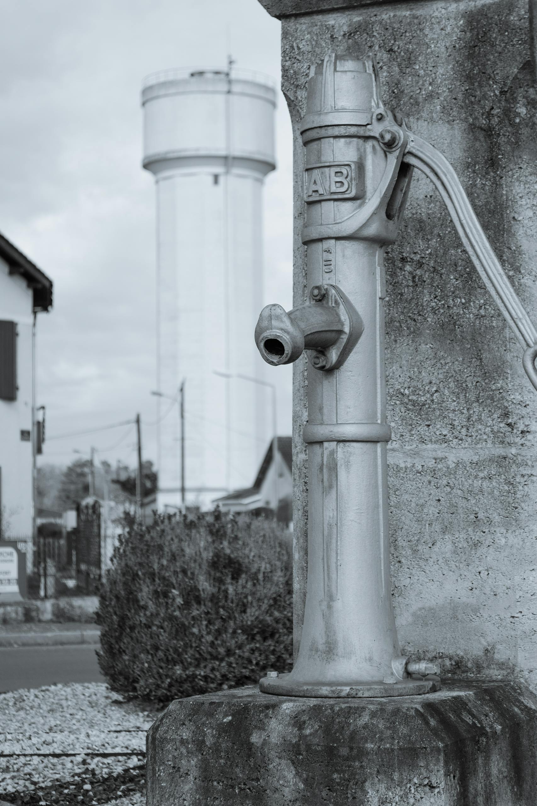 A vintage water pump with a water tower in Saint-Aigulin, France, illustrating rustic charm.