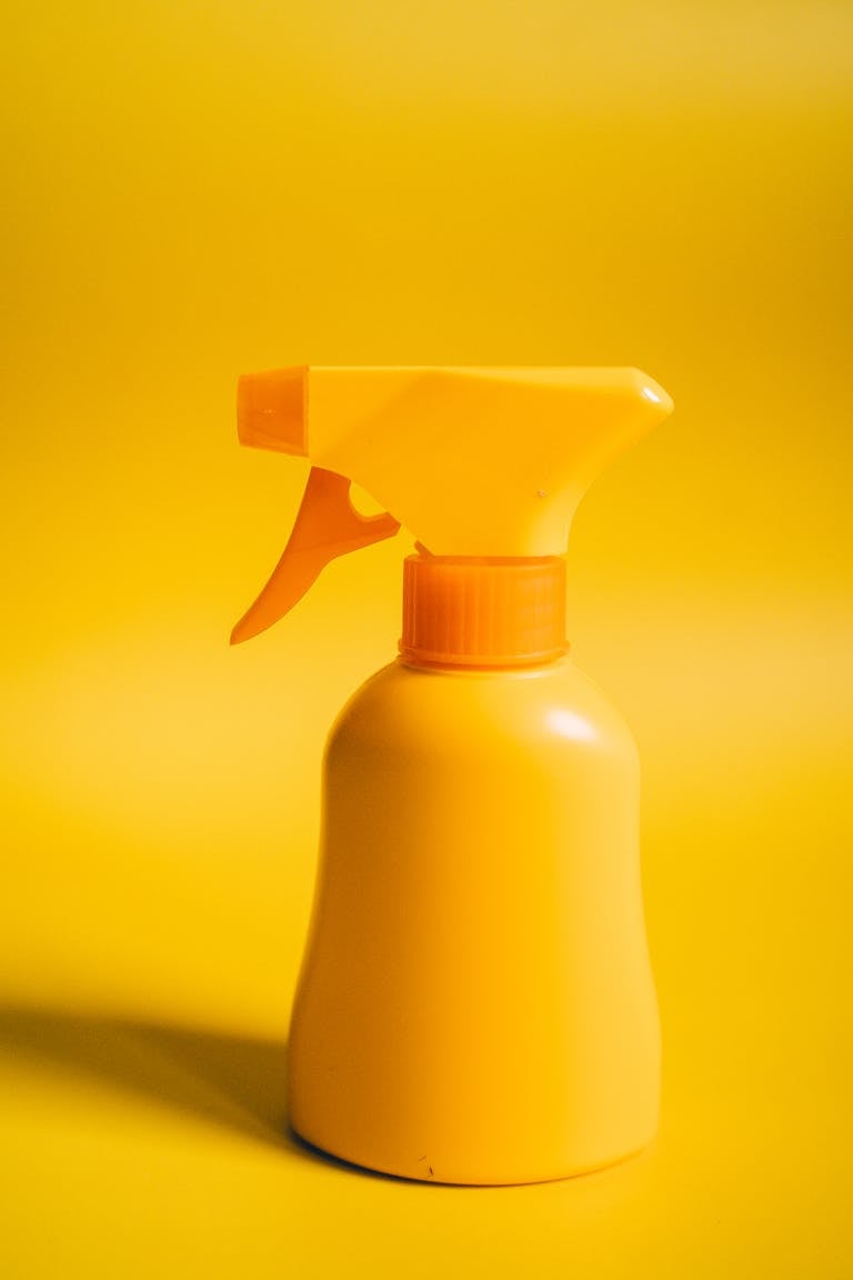 Bright yellow spray bottle against a matching yellow backdrop, perfect for product or cleaning themes.