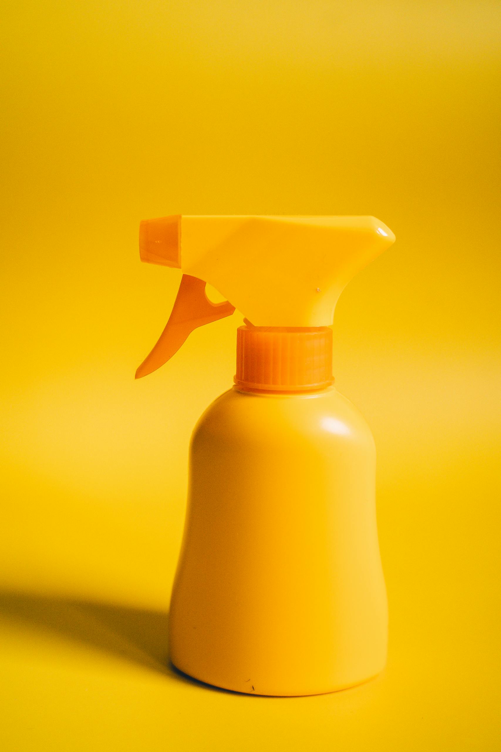 Bright yellow spray bottle against a matching yellow backdrop, perfect for product or cleaning themes.
