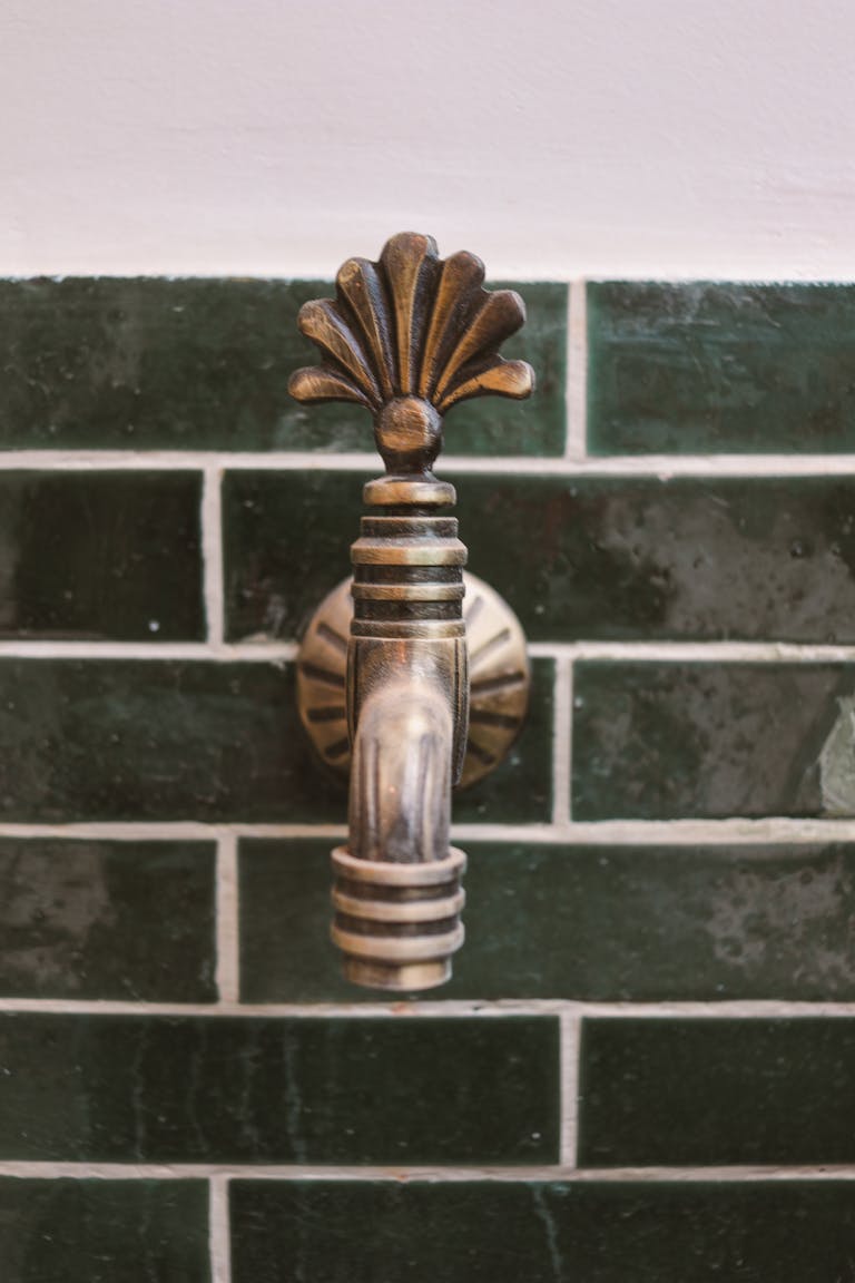 Close-up of a decorative brass faucet on a dark green tiled wall, evoking a vintage aesthetic.