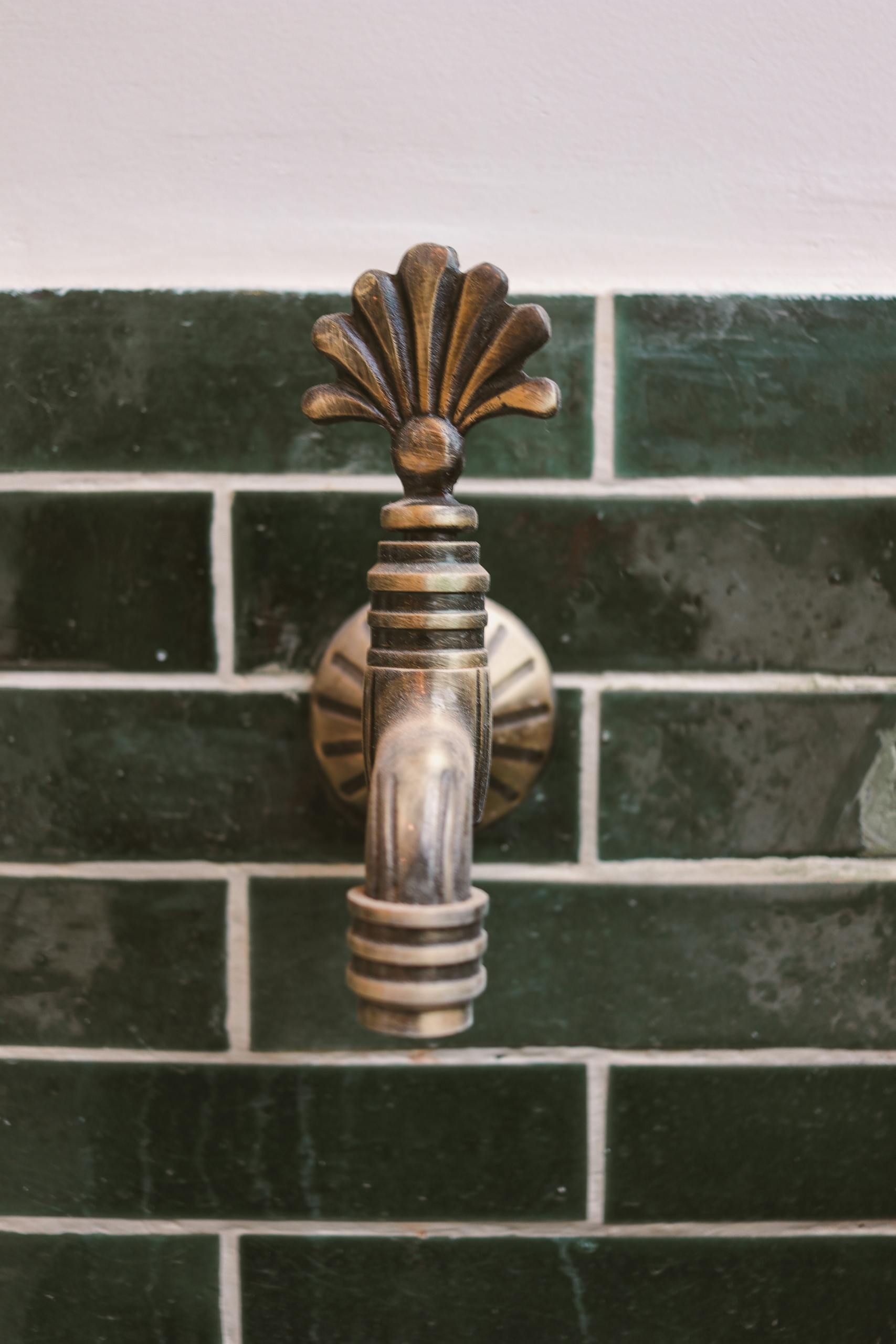 Close-up of a decorative brass faucet on a dark green tiled wall, evoking a vintage aesthetic.