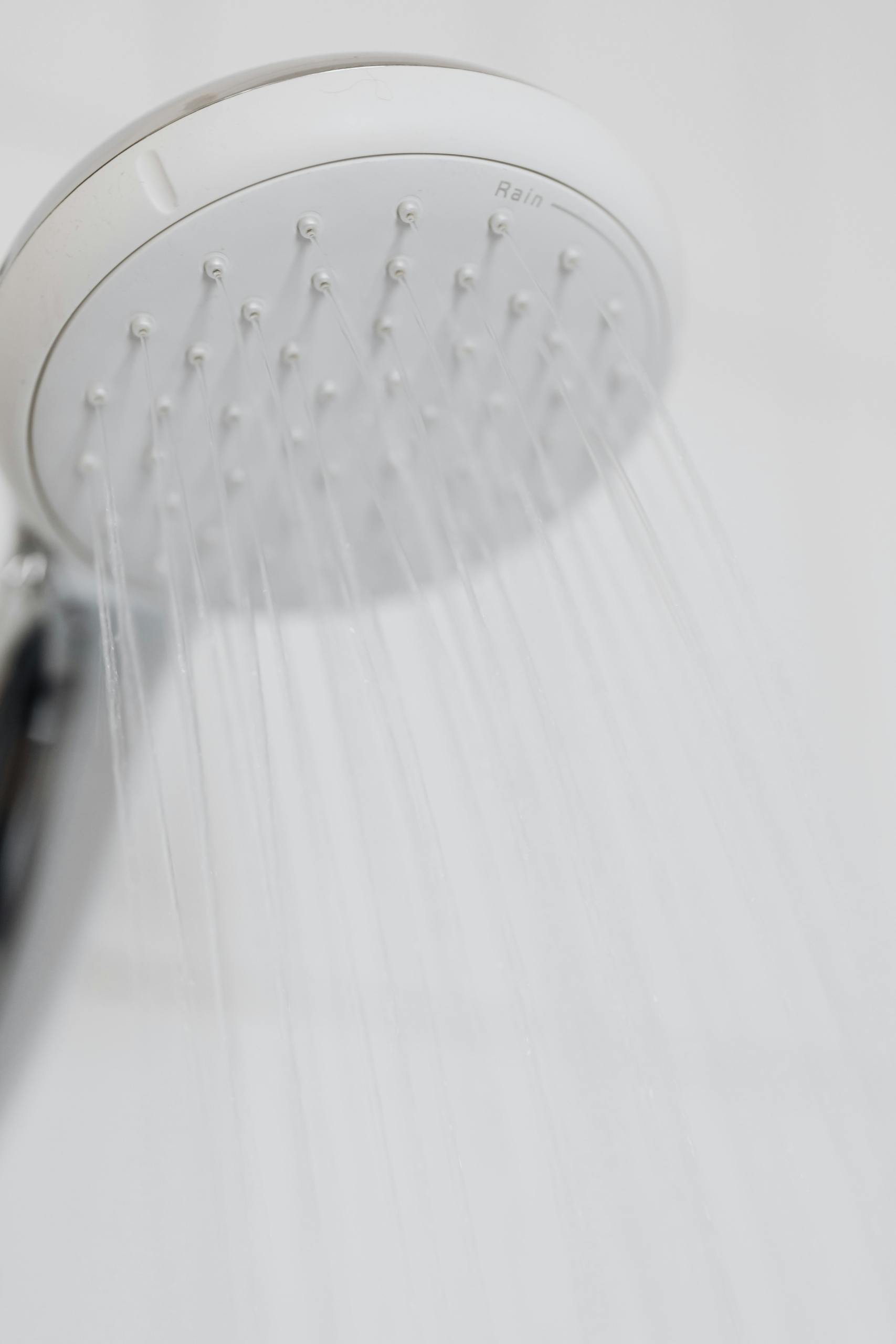 Close-up of a modern shower head with water streaming in a white bathroom setting.