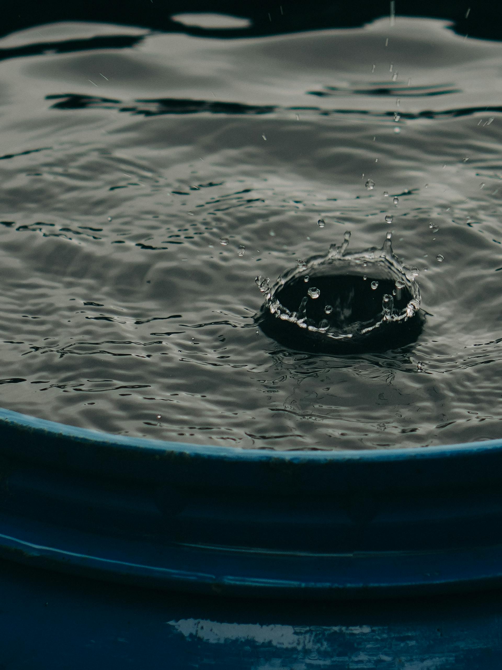 Close-up of a water droplet creating a splash in a blue barrel, capturing the motion in detail.
