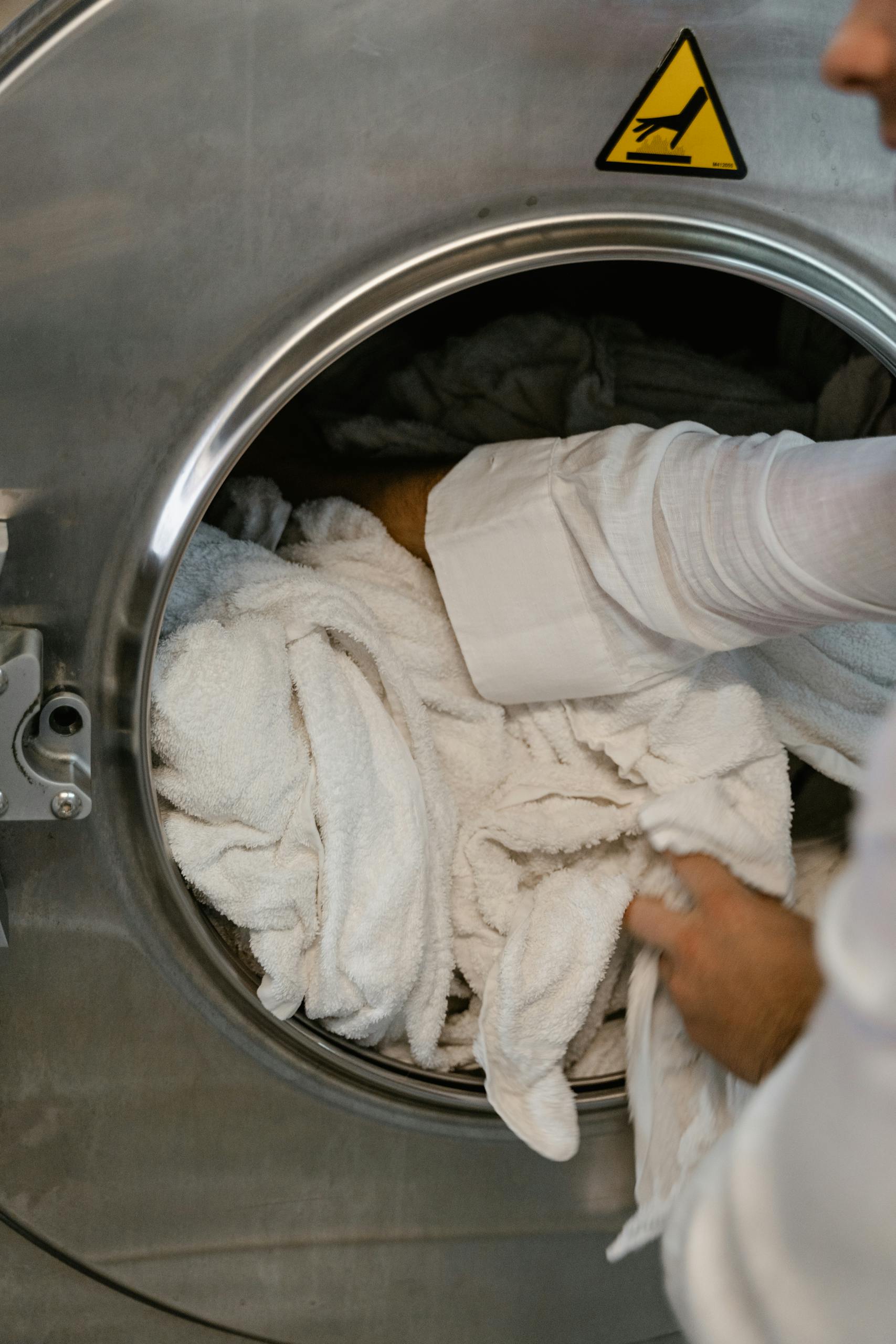 Close-up of hands loading white towels into a large industrial washing machine at a laundromat.