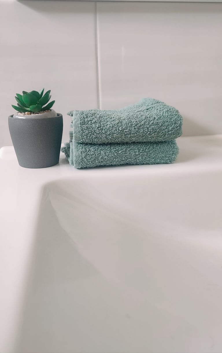 Elegant bathroom setup featuring a stacked teal towel and a faux succulent plant in a gray pot.