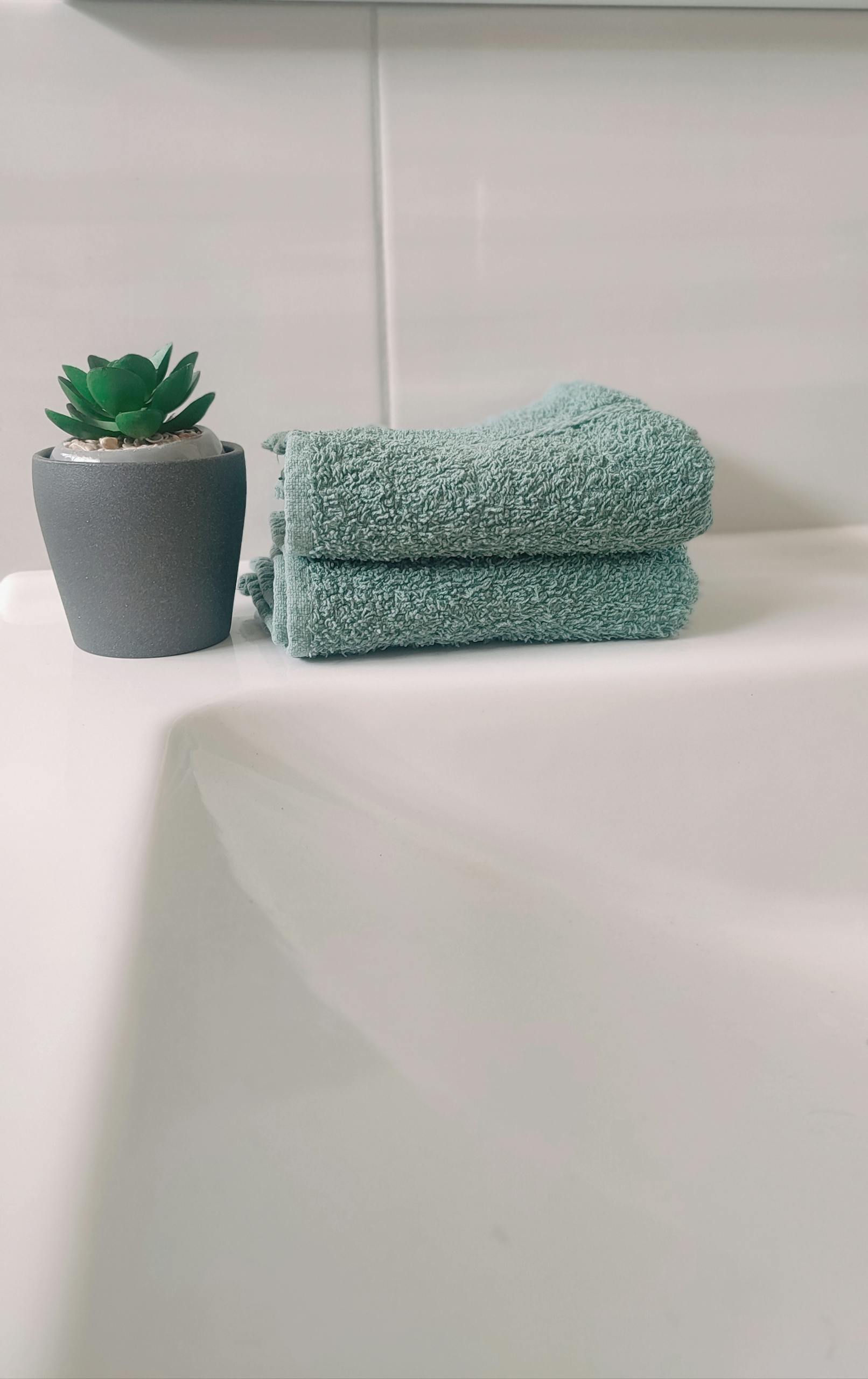 Elegant bathroom setup featuring a stacked teal towel and a faux succulent plant in a gray pot.