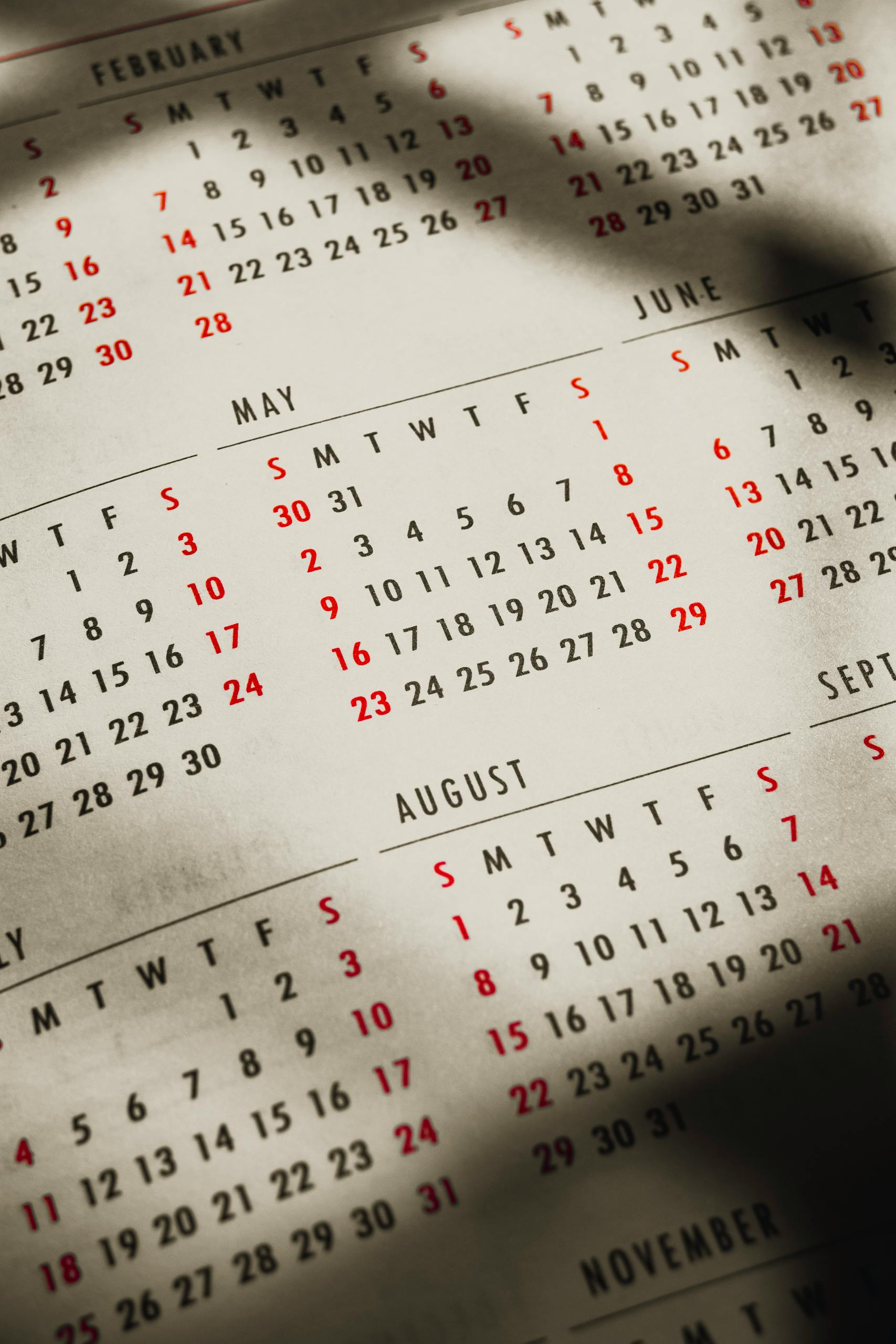 From above of shadows on paper calendar with month inscriptions and dates on sunny day