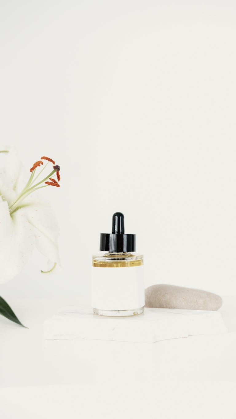 Minimalist skincare bottle and white lily on soft background, offering elegant product presentation.