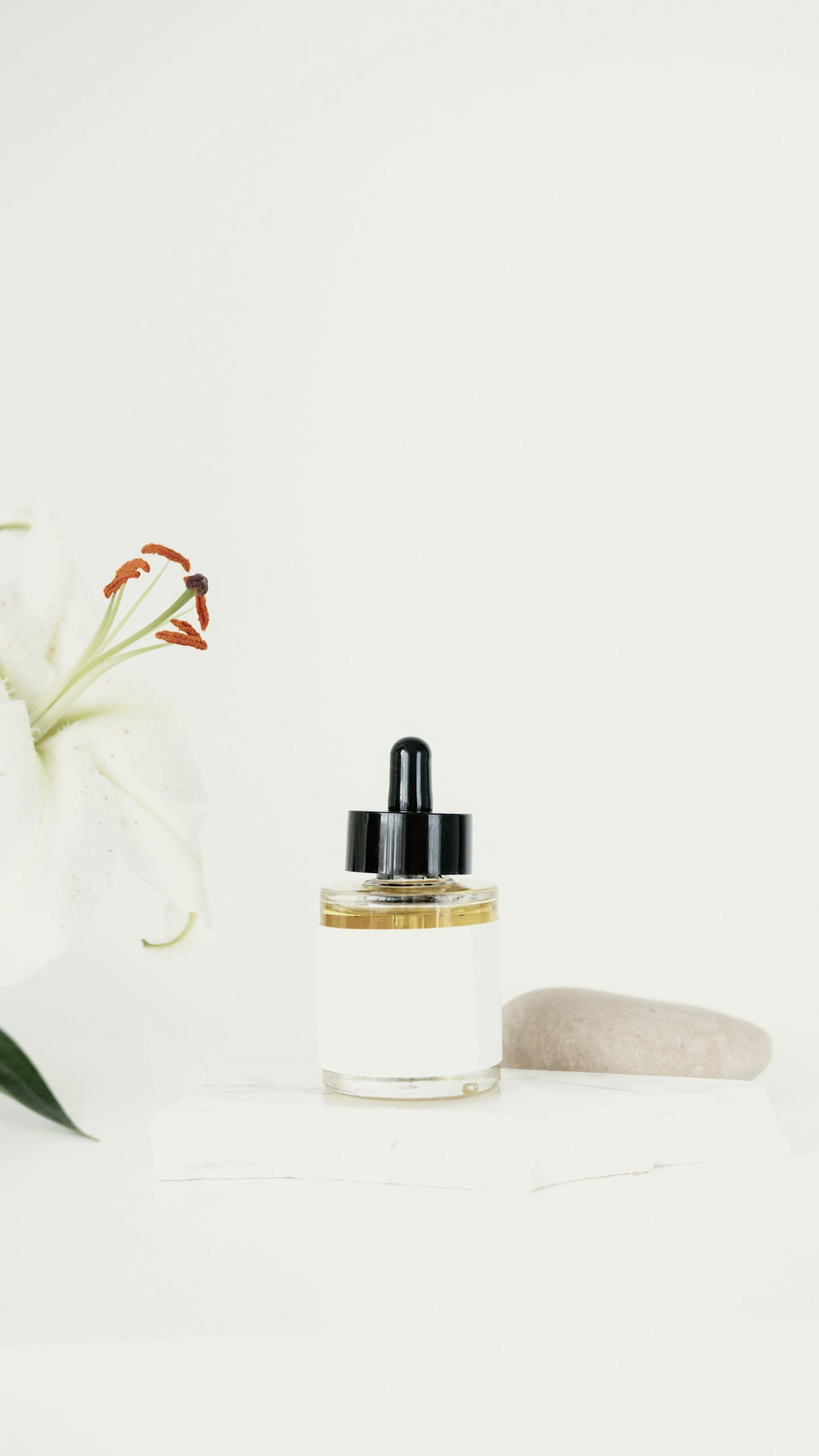 Minimalist skincare bottle and white lily on soft background, offering elegant product presentation.