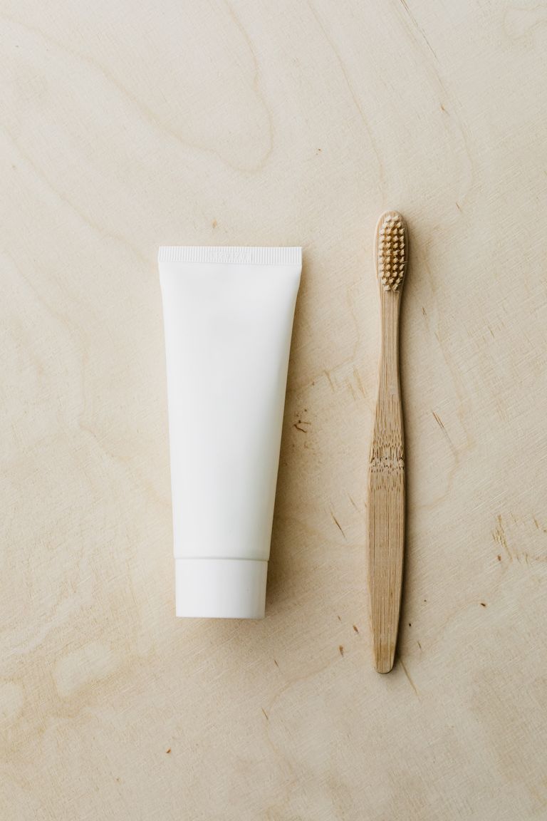 Top view of white mockup toothpaste tube and bamboo toothbrush placed on light brown wooden surface