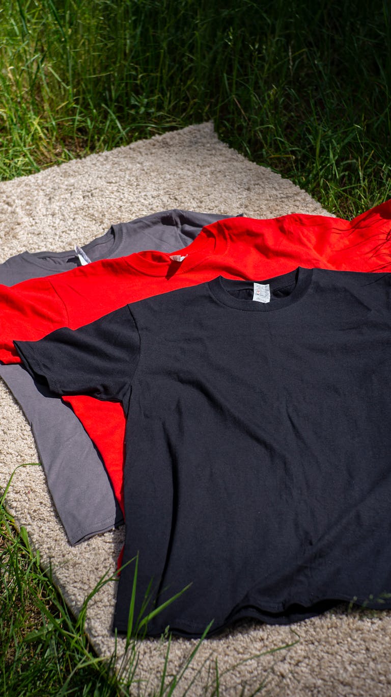 Various colored T-shirts laid on grass, showcasing fashion options.
