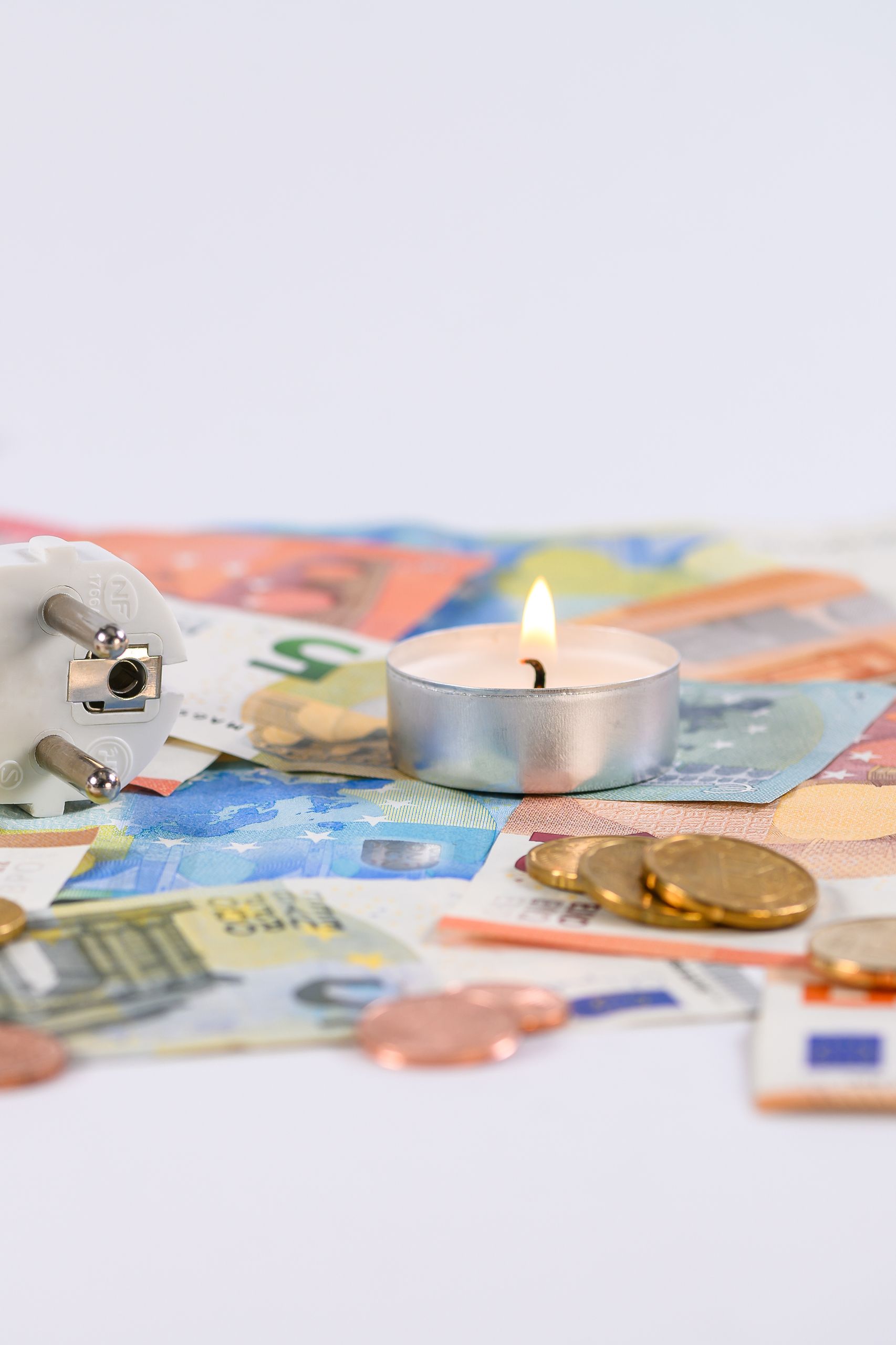 A burning candle on Euro money with a power plug symbolizing energy costs.