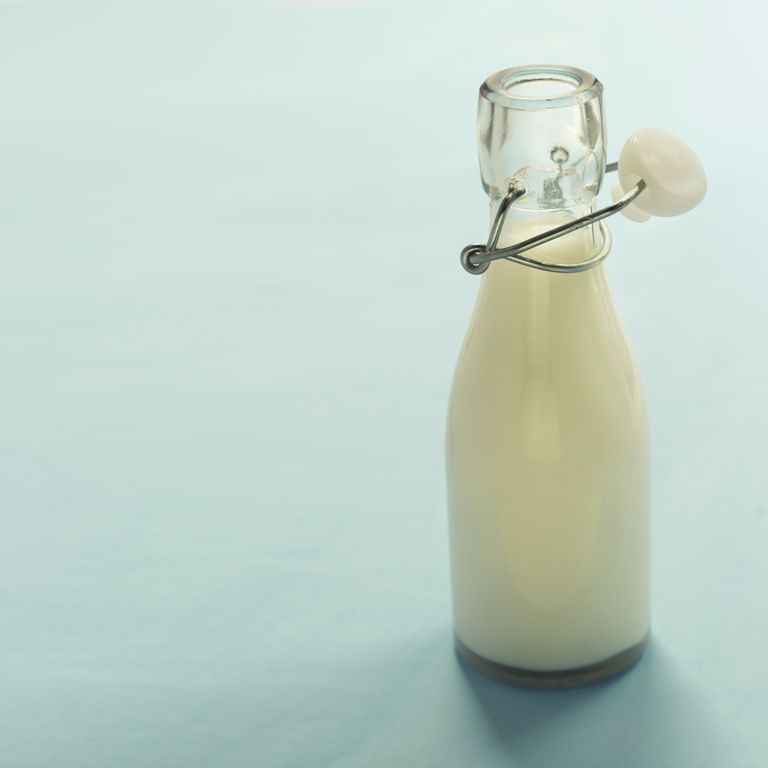 A minimalist image of a glass bottle filled with milk on a light blue background, offering ample copyspace.