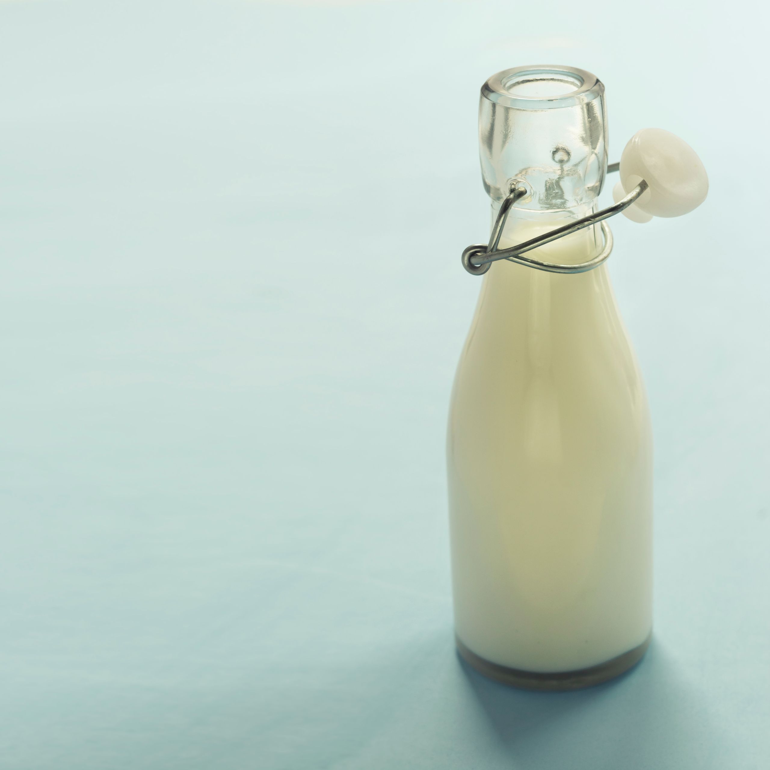 A minimalist image of a glass bottle filled with milk on a light blue background, offering ample copyspace.