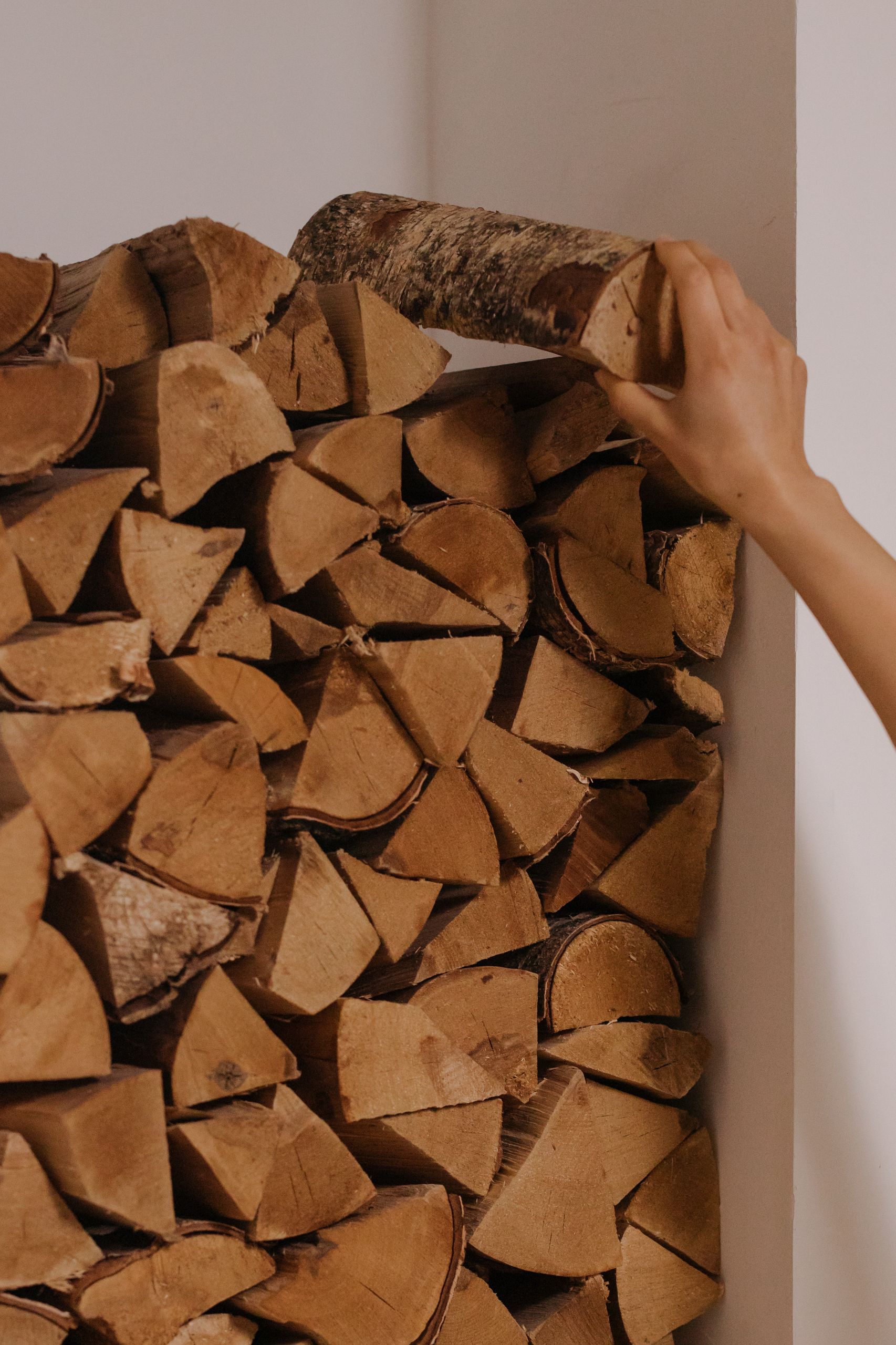 Close-up of a hand stacking firewood logs indoors, creating a neat pile.
