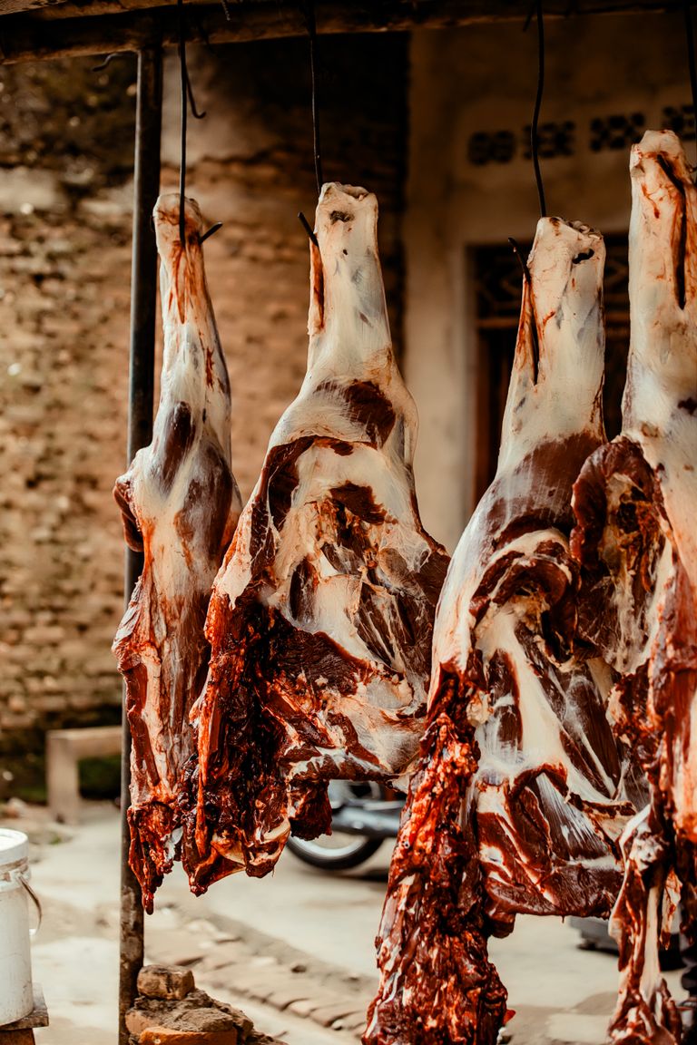 Close-up of butchered animal carcasses hanging in an outdoor market setting.
