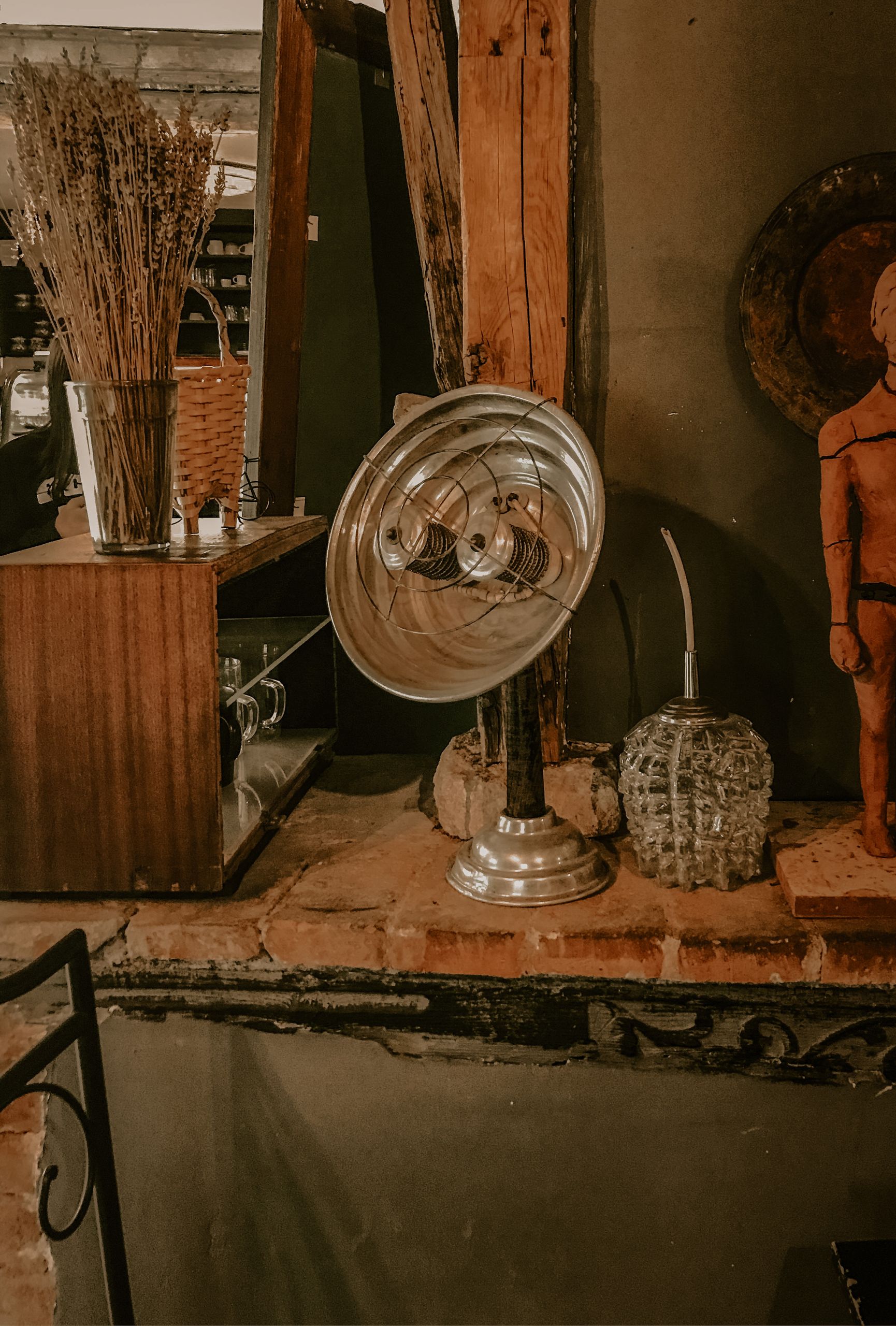 Reflector with heated spiral placed on shelf near bunch of dry twigs in vase in market with old fashioned goods